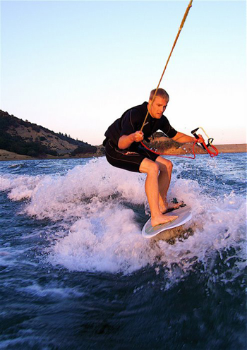 Joel surfing on the back of a boat on the lake.