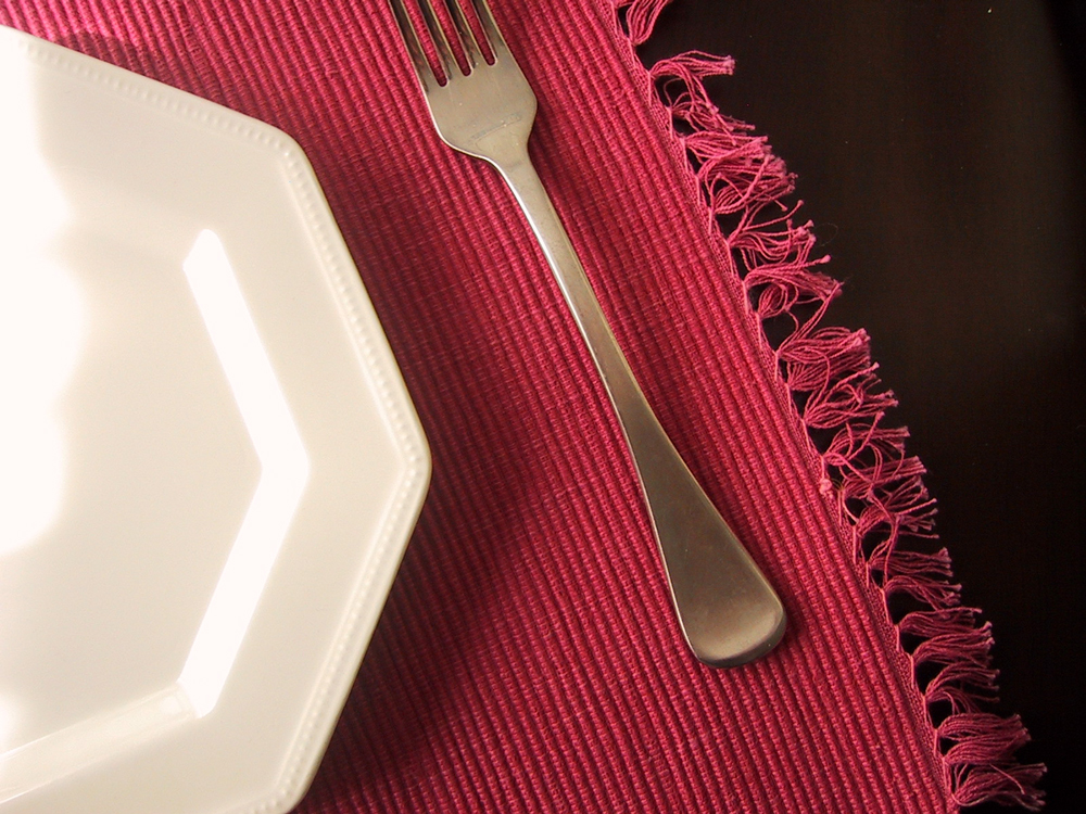 Dinner plate and a fork on a pink woven place mat.