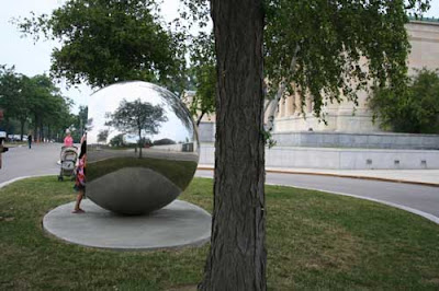 Large mirrored sphere, reflecting a tree, the sky and grass.