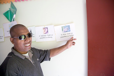 Roddy Robert in dark glasses pointing to information on a school wall