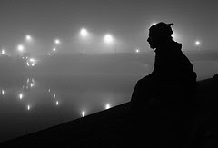 Silhouette of a man on a hill, in fog with lights behind