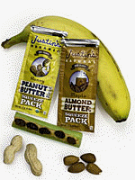 picture of two packages of Justin's Nut Butter, four peanuts, two almonds, and two bananas on a gray background